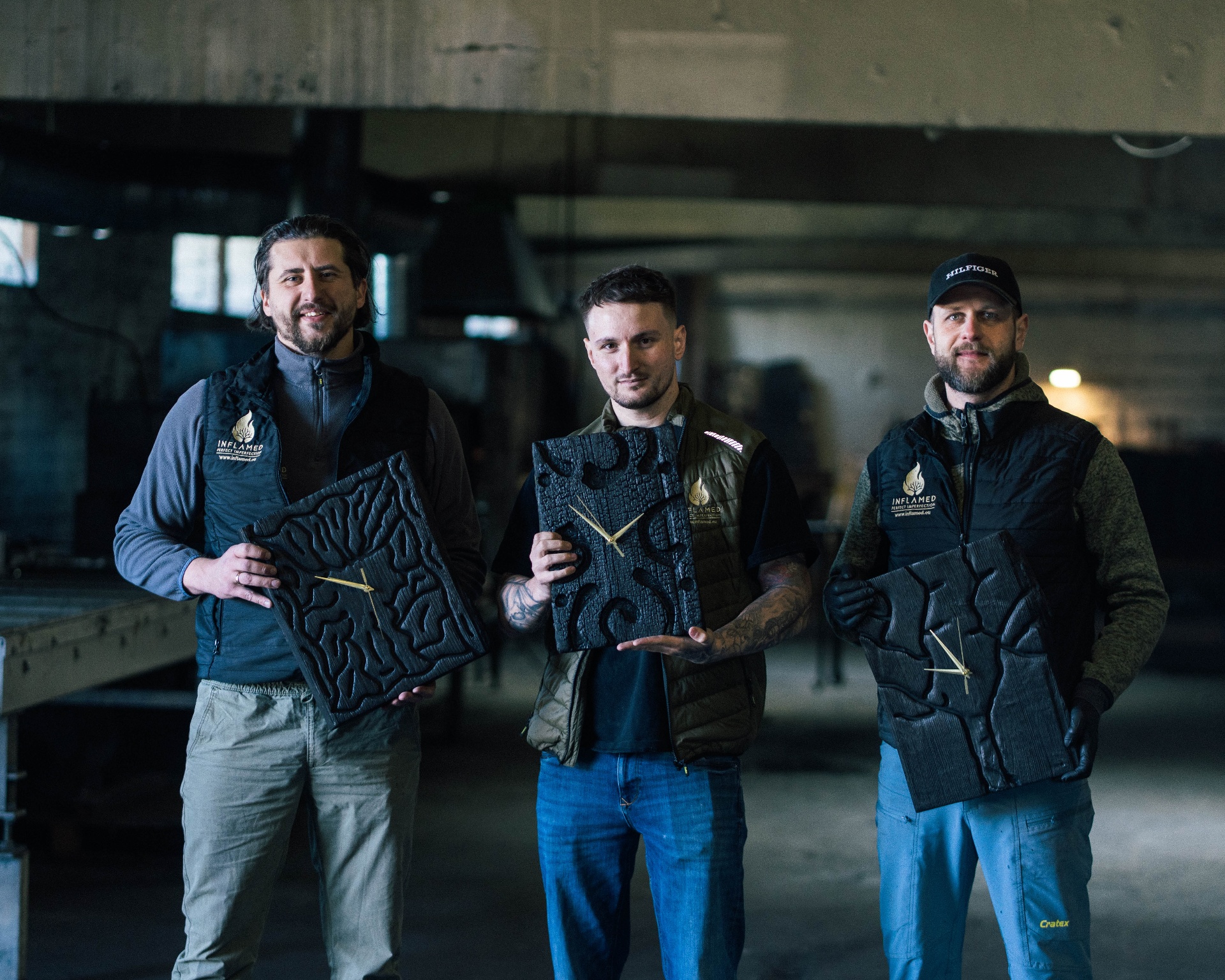 The Ember & Oak makers in their Lithuanian workshop holding finished charred oak clocks